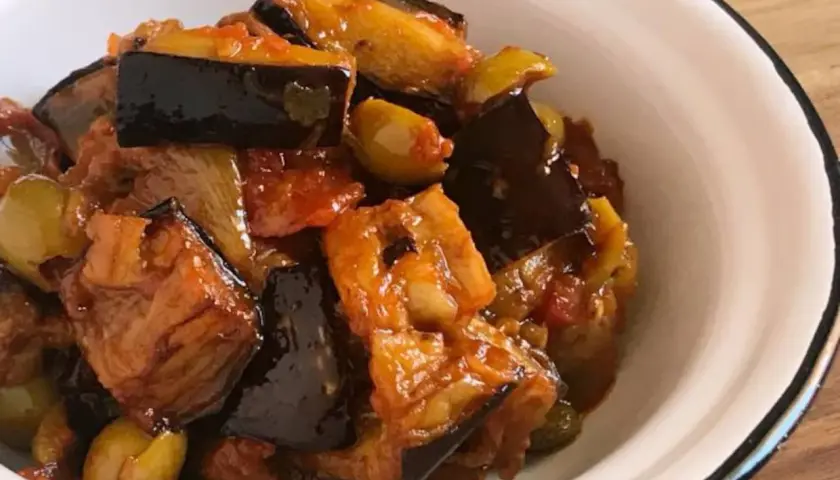 Caponata que es: un delicioso guiso siciliano de berenjenas, aceitunas y tomate, servido en un cuenco blanco.