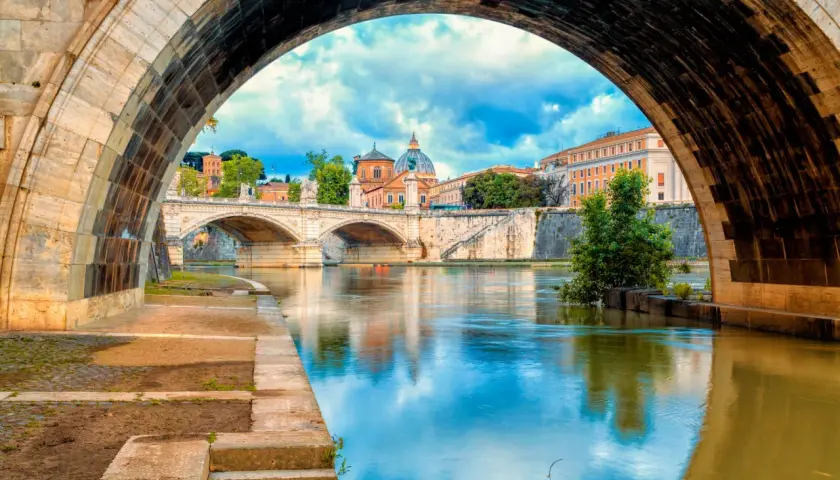 Ponte Sant'Angelo e il Tevere, un'icona di cosa vedere a Roma. La cupola di San Pietro si riflette sull'acqua.