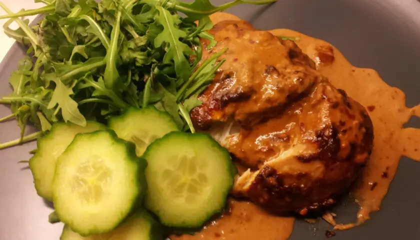 Kyckling i krämig sås med sambal oelek, serverad med ruccola och gurkskivor.