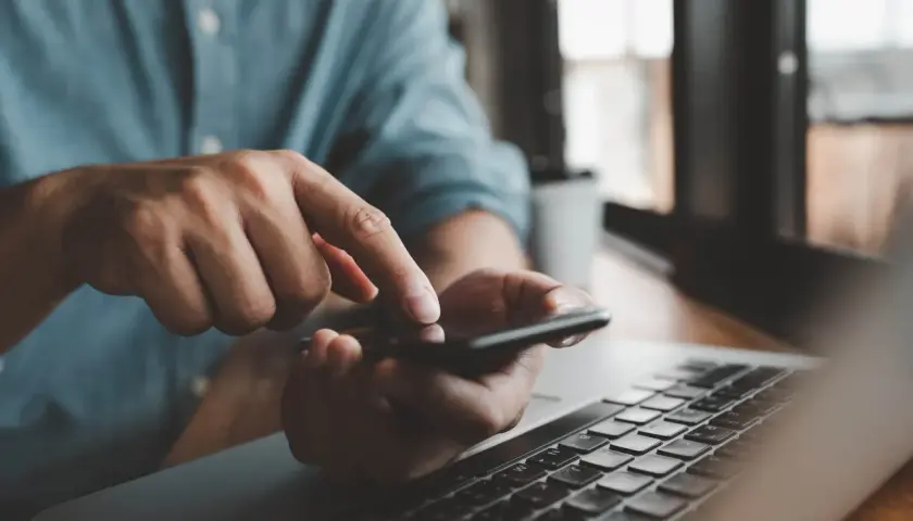 Mężczyzna sprawdza na telefonie, czy lokator może zawrzeć umowę na prąd, obok leży laptop.