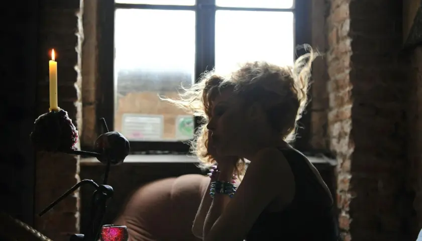 Silhouette of a woman with curly hair, looking down, with a lit candle and a window in the background.