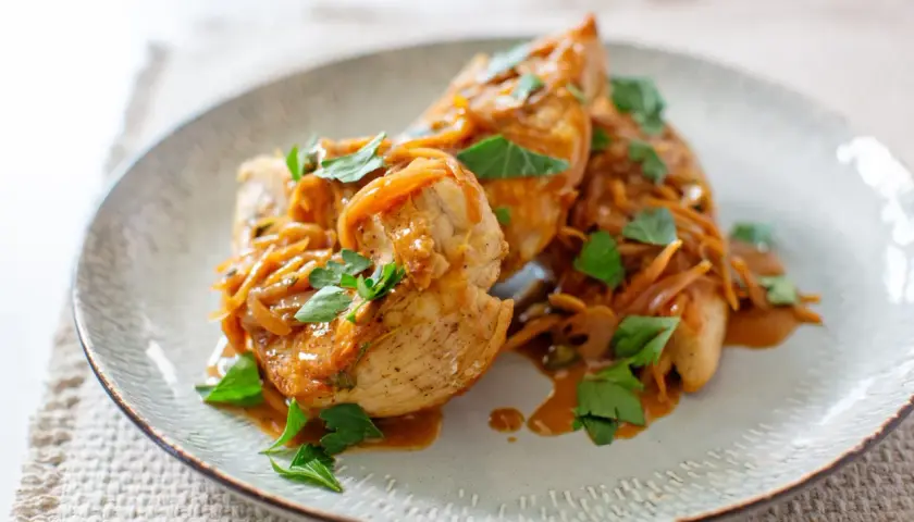 Délicieux sauté de poulet servi sur une assiette, garni d'oignons caramélisés et de persil frais.
