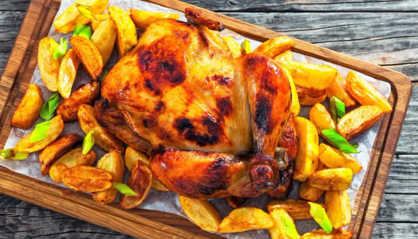 Un poulet rôti doré et croustillant, entouré de pommes de terre rôties et d'oignons verts, prêt à être dégusté.