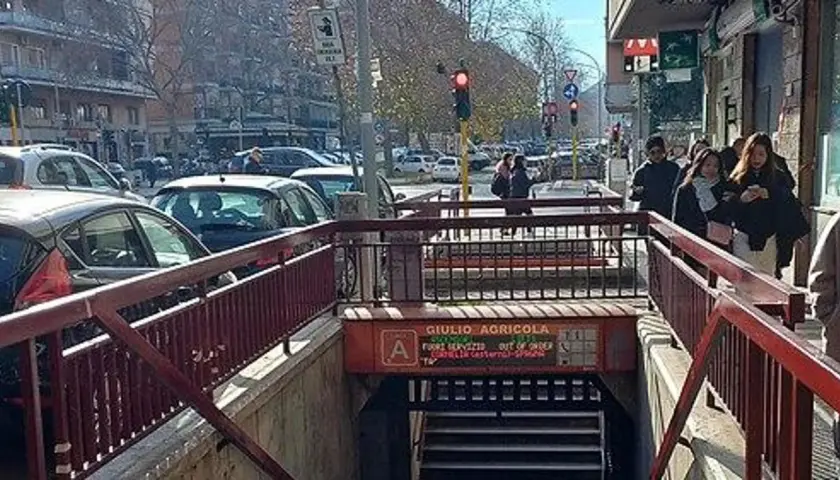 Ingresso della fermata Giulio Agricola della metro A, con persone che camminano e traffico in strada.