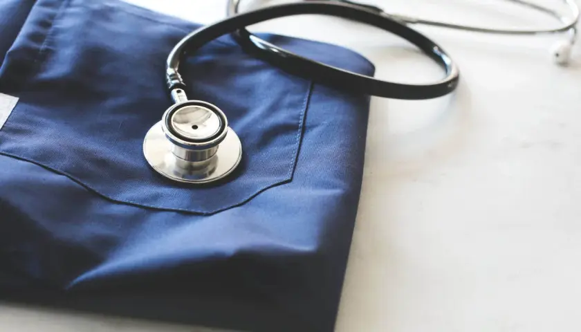 Un camice blu e uno stetoscopio appoggiati su un piano bianco. Immagine evocativa per chi vuole capire come diventare guardia medica.