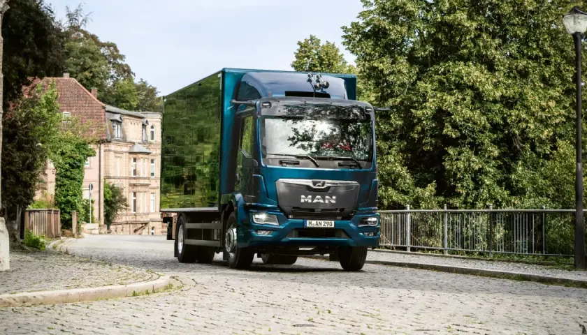 Camion MAN bleu turquoise avec remorque verte sur une route pavée.