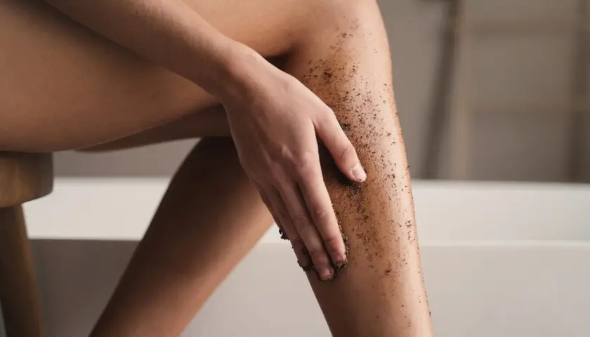 Kobieta wykonuje peeling kawowy na nogach, przygotowując skórę do golenia.