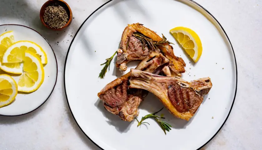 Trois côtelettes d'agneau grillées, garnies de romarin et de citron, prêtes pour le temps de cuisson idéal.