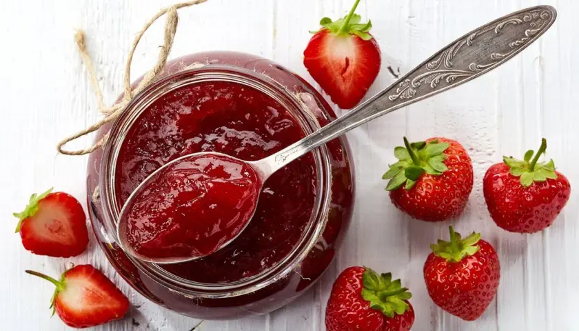 Un vasetto di marmellata di fragole fatto in casa, con fragole fresche e un cucchiaio pieno di dolcezza rossa.