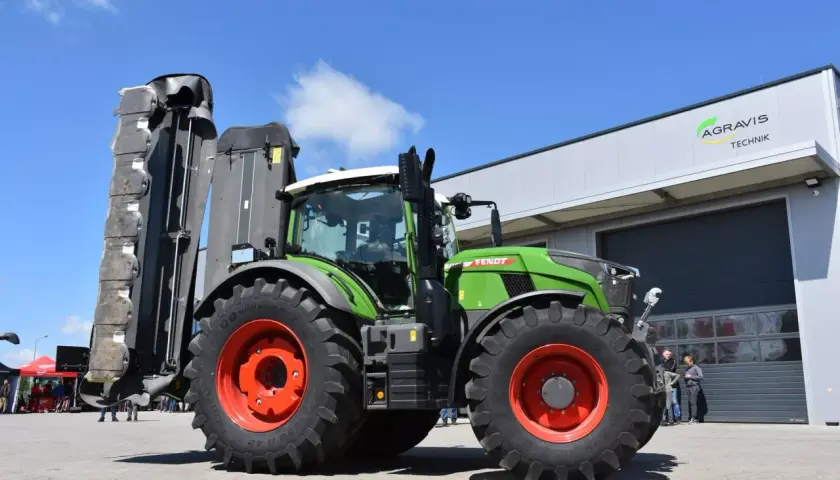 Zielony traktor Fendt 724 Vario z zamontowaną kosiarką, gotowy do pracy na polu.