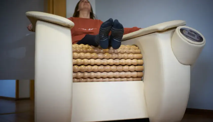 Kobieta relaksuje się na fotelu z masażem rolletic. Drewniane rolki masują jej nogi, podczas gdy ona unosi głowę do góry.