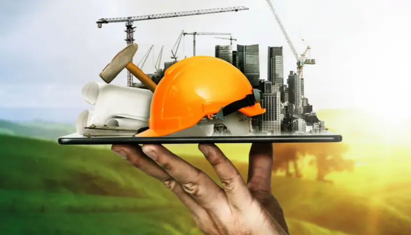 Dłoń trzyma tablet z budowlanymi symbolami: kask, młotek, plany, dźwigi i miasto.