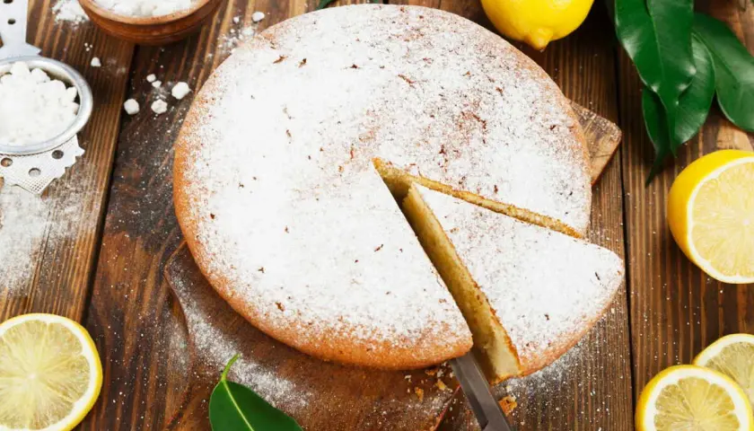 Un délicieux gâteau italien au limoncello, saupoudré de sucre glace, avec des citrons frais et des feuilles vertes sur fond de bois.