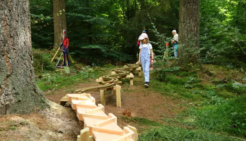 Ein Mädchen erkundet den erlebnispfad eifel kinder. Holzrinnen und eine Spielzeugbahn schlängeln sich durch den Wald.