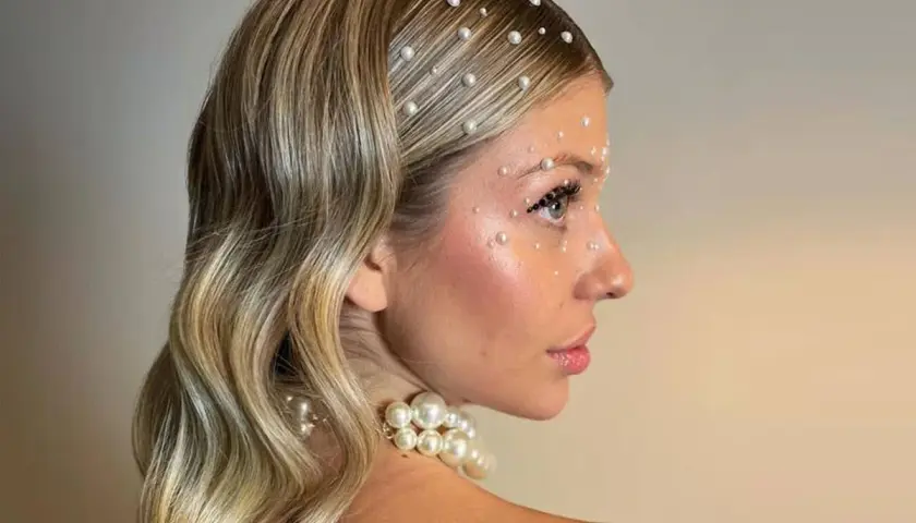 Peinados para salir de fiesta: melena rubia ondulada adornada con perlas en el cabello y rostro, look deslumbrante.