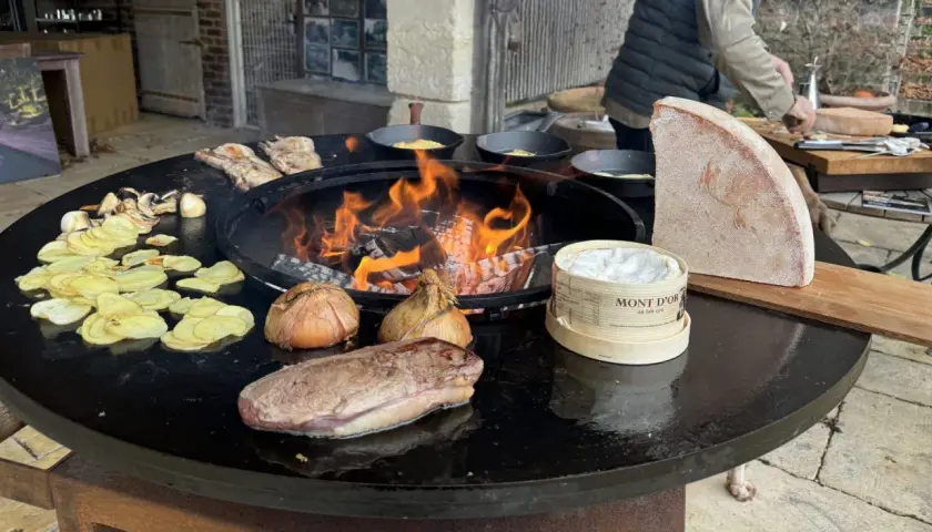 Préparation d'une recette brasero hiver : viande, pommes de terre, oignons, champignons et Mont d'Or fondent sur le feu.