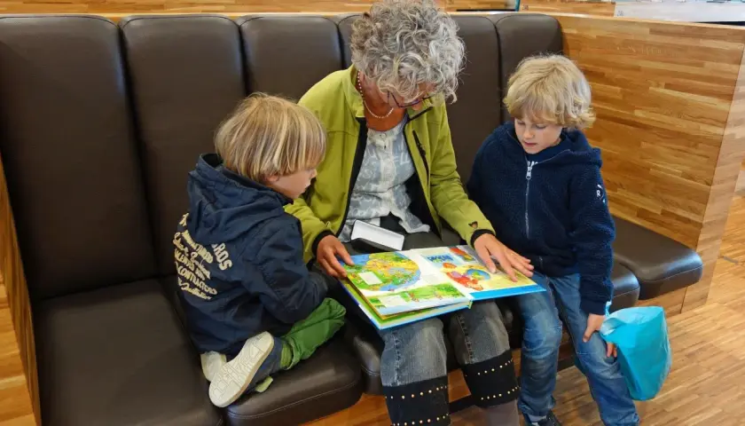 Oma und Enkel sitzen auf einer Bank und lesen gemeinsam ein buntes Bilderbuch.