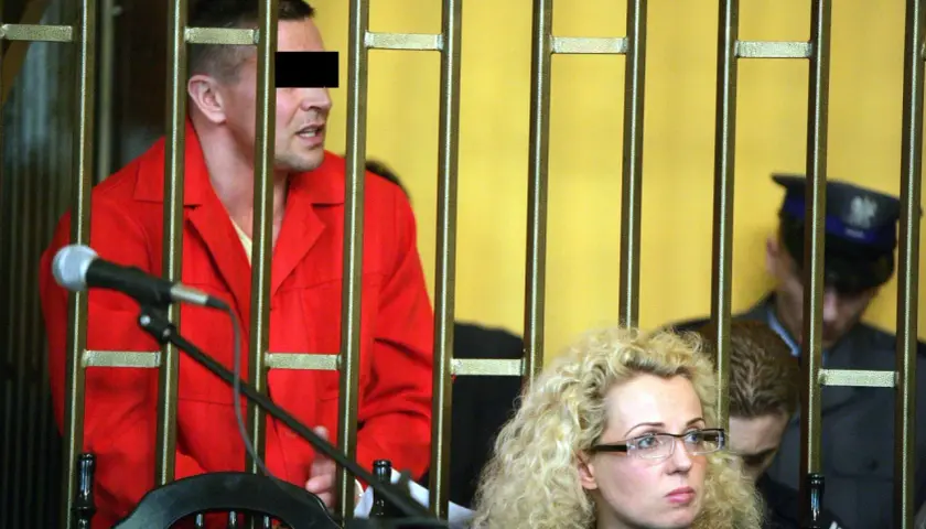 Mężczyzna w czerwonym ubraniu, przypominający lelek gangster, za kratami. Obok kobieta w okularach i policjant.