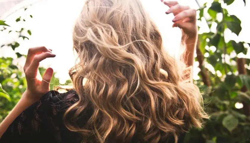 Cabello rubio con reflejos naturales, como si fuera babylights vs balayage. Manos en el aire, rodeada de vegetación.
