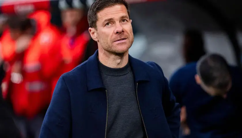 Xabi Alonso, potencjalny trener Chelsea, w granatowej kurtce i szarym swetrze, z uwagą obserwuje boisko.