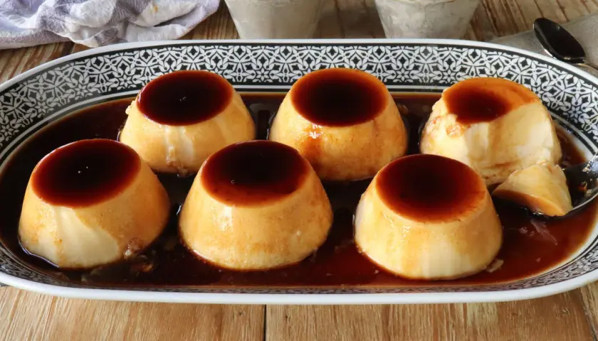 Seis deliciosos flanes de leche condensada, bañados en caramelo líquido, servidos en una bandeja decorada.