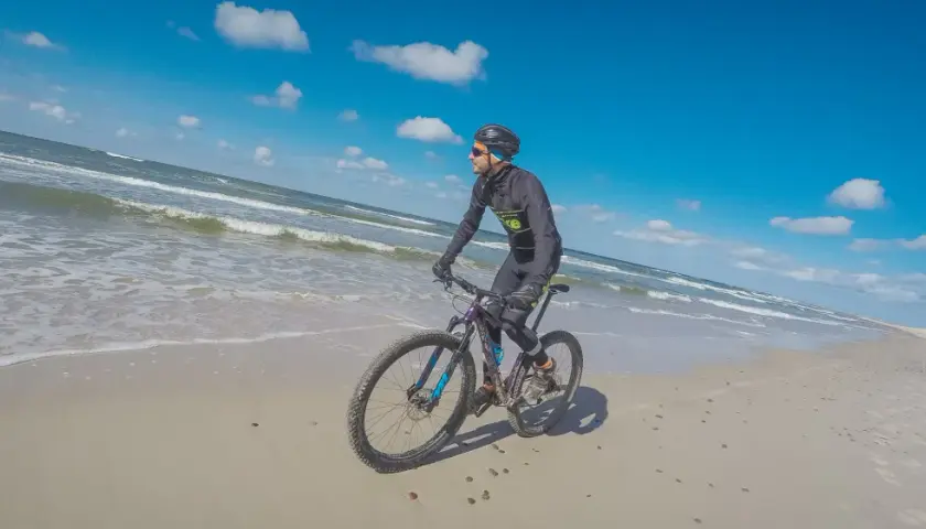 Rowerzysta przemierza piaszczyste plaże Słowińskiego Parku Narodowego. W tle błękitne niebo i fale Bałtyku.
