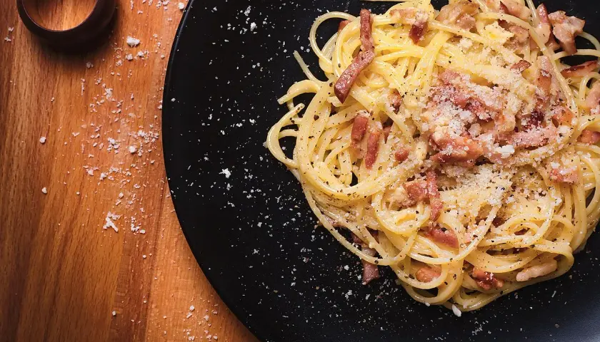 Un plat de spaghetti à la carbonara, garni de lardons et de parmesan râpé, prêt à être dégusté. Parfait pour des recettes pâtes à la carbonara.