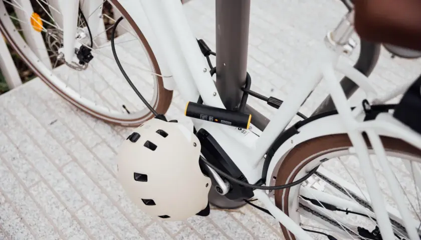 Biały rower zabezpieczony U-lockiem. Kask rowerowy wisi na ramie. Zastanawiasz się, jak otworzyć zapięcie do roweru bez klucza?