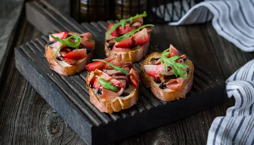 Bruschetta z truskawkami i szynką prosciutto, polana balsamicznym sosem. Idealny przepis na letnią przekąskę.