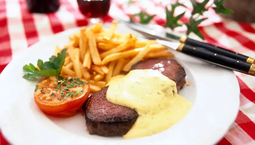 En tallrik med saftig steak frites, gyllene pommes frites, en ugnsbakad tomat och en krämig sås. En klassisk måltid!