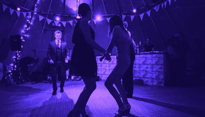 Tańczący ludzie na weselu przy świetle fioletowych lamp. Idealna playlista na wesele sprawia, że wszyscy bawią się świetnie.