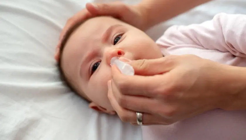 Mani che aiutano un neonato di 2 mesi con la tosse, somministrando gocce nasali per alleviare il naso chiuso.