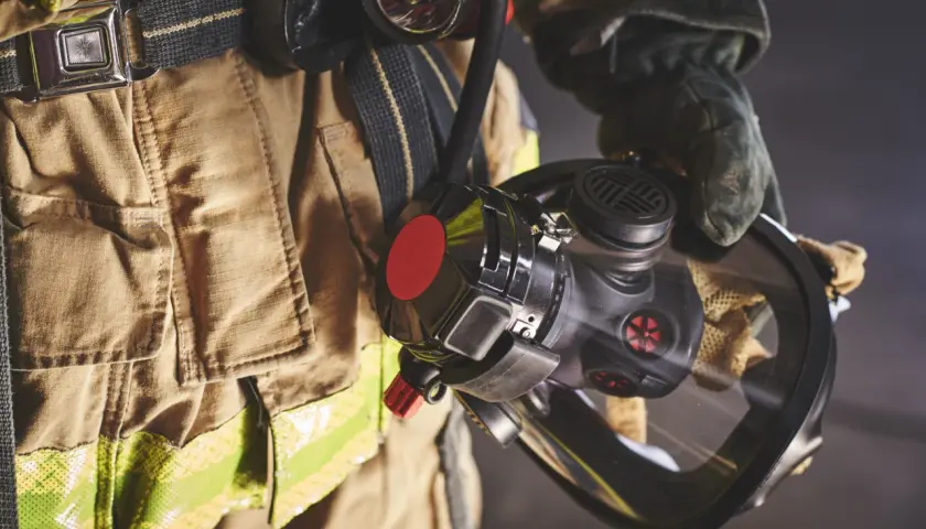 Bombero con equipo de protección, incluyendo una máscara y un compresor de aire respirable.
