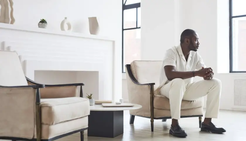 Un homme élégant en tenue claire, assis dans un fauteuil, montre comment porter des mocassins avec style.