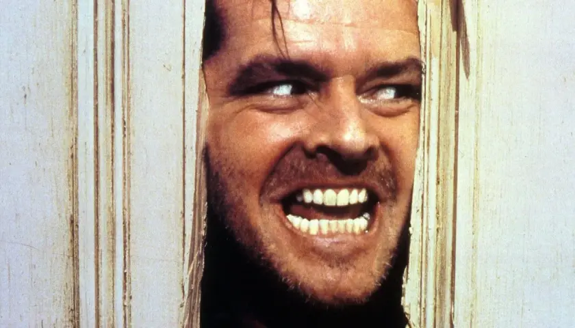 Jack Nicholson, con occhi bianchi e sorriso folle, sfonda una porta. Il suo volto è il **shining significato finale** di un incubo.