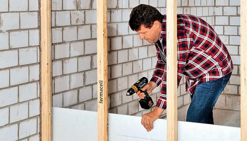 Mann baut eine Trockenbauwand mit Akkuschrauber und Gipskartonplatten.