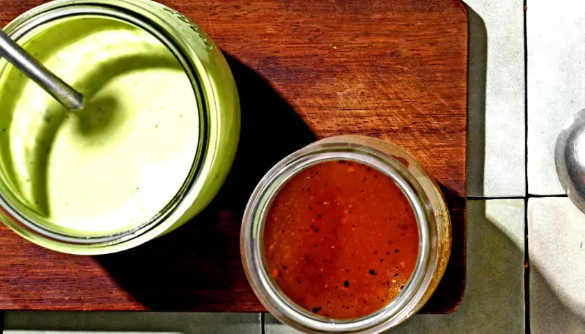 Zwei Gläser mit Saucen: ein cremiges Avocado Dressing für Salat und eine rote Vinaigrette.