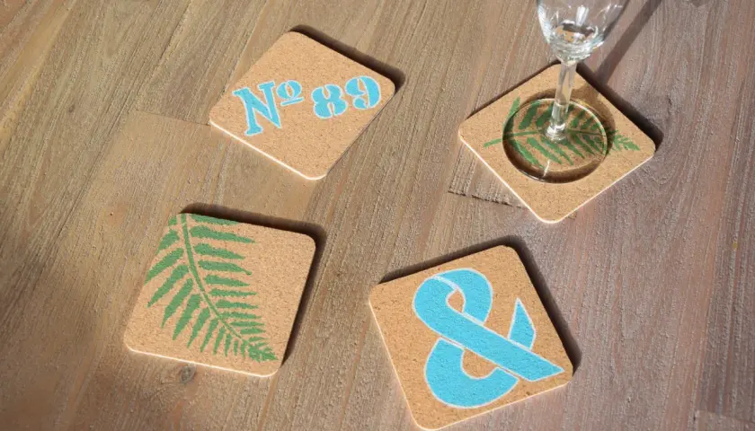 Vier bemalte Bierdeckel mit Farnblatt, Ampersand und "Nº 89" in Blau und Grün auf Holz.