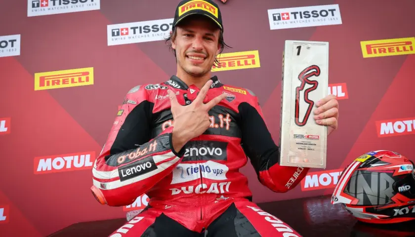 Nicolò Bulega, piloto de Ducati, celebra su victoria en Motorland Aragón con el trofeo y haciendo la señal de la victoria.