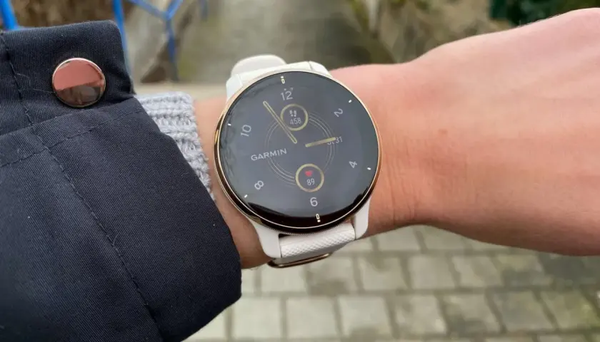 Biały zegarek Garmin na nadgarstku, z widocznym tętnem i liczbą kroków.