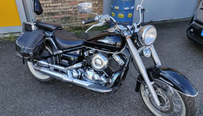 Yamaha Dragstar 650 Custom nera, con borse in pelle borchiate e pneumatici a banda bianca, pronta per un viaggio.