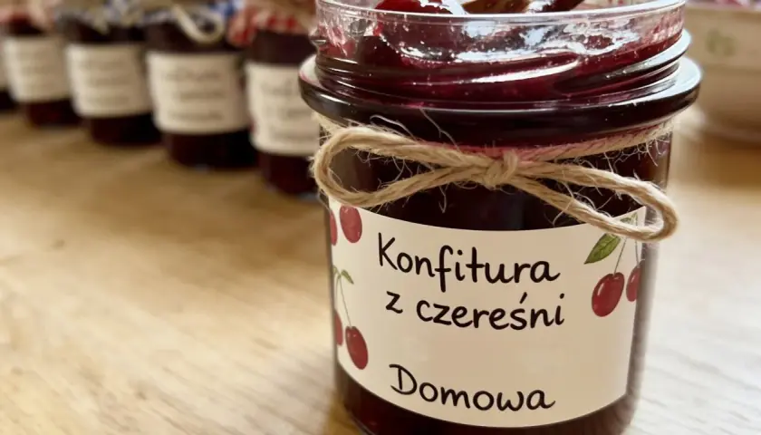 Słoik z domową konfiturą z czereśni, ozdobiony sznurkiem i etykietą z rysunkiem owoców.