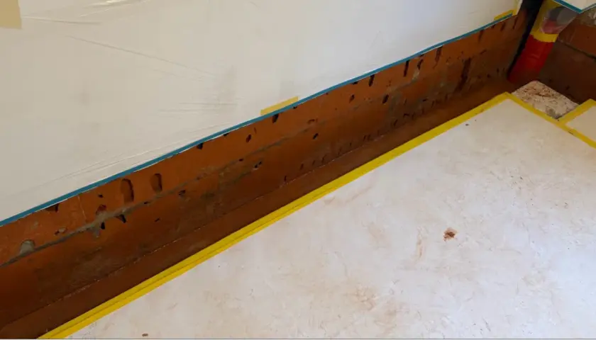 Vorbereitung für die Kellerabdichtung: weiße Folie schützt Wand, gelbes Band markiert den Bereich.