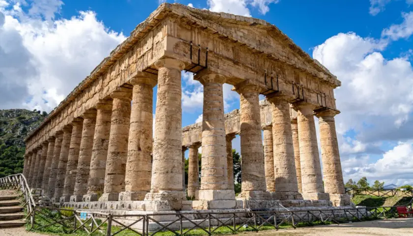 Ancient Greek temple ruins, a highlight of a 2 week Sicily itinerary, stand majestically under a blue, cloudy sky.