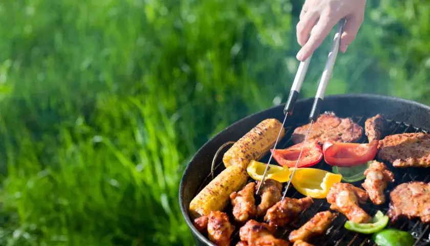 Un barbecue sain en plein air avec des épis de maïs, des poivrons colorés et des brochettes de poulet grillant sur le feu.