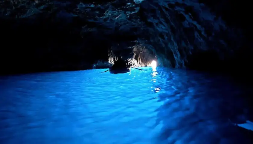 Barca a remi naviga nelle acque azzurre della grotta dello smeraldo, illuminata dalla luce che filtra dall'esterno.