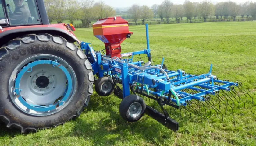Tracteur rouge avec semoir bleu pour le sursemis de prairie. L'outil prépare le sol avant de semer de nouvelles herbes.