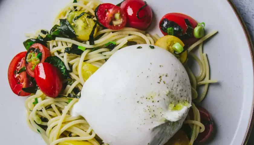Une belle recette burrata avec des pâtes, des tomates cerises rouges et jaunes, et des herbes fraîches.