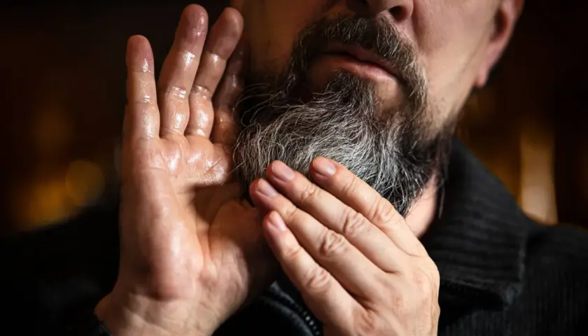 Mężczyzna z siwiejącym zarostem delikatnie dotyka dłonią brody, pokazując jak zapuszczać zarost i dbać o niego.