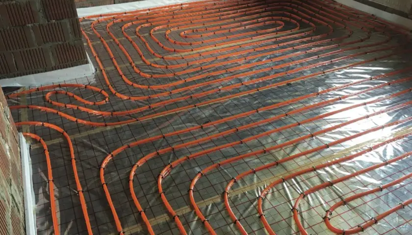 Pomarańczowe rury ogrzewania podłogowego ułożone na folii i siatce. To kluczowy etap prac, zapewniający izolację poziomą chudziaka.